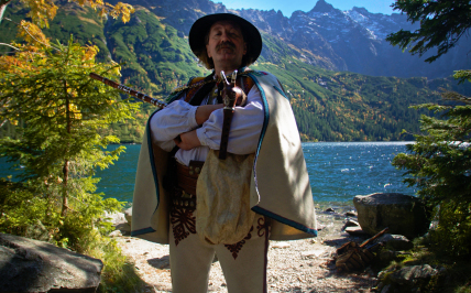 mężczyzna w stroju góralskim stoi przy jeziorze
