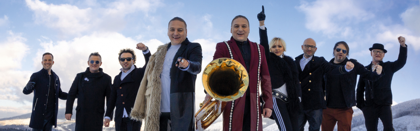 Grupa ludzi z instrumentami muzycznymi pozuje na zaśnieżonej łące