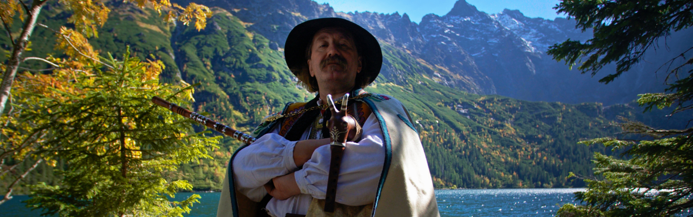 mężczyzna w stroju góralskim stoi przy jeziorze