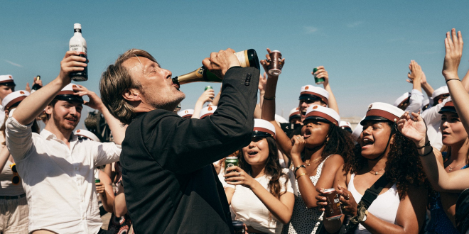 Mężczyzna pije z butelki, wokół niego stoi wiwatujący tłum