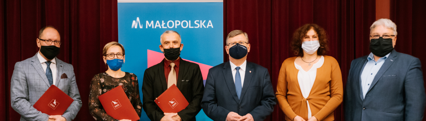 Dwie kobiety i czterech mężczyzn w maseczkach na twarzy stoi na tle roll-upa Małopolski