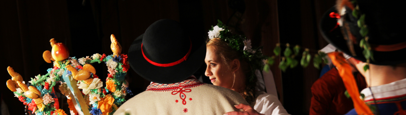 Kobieta i mężczyzna w strojach regionalnych trzymają w rękach różdżkę weselną