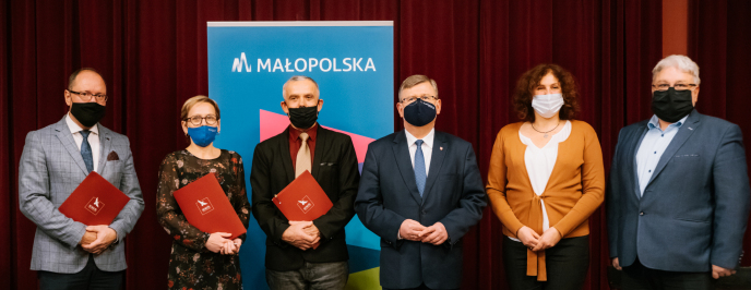 Dwie kobiety i czterech mężczyzn w maseczkach na twarzy stoi na tle roll-upa Małopolski