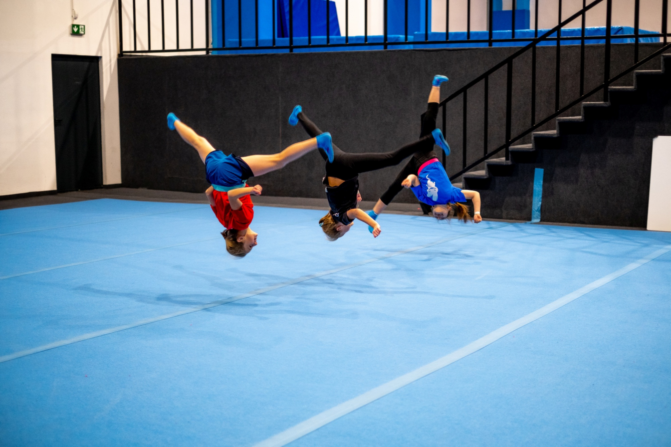 Troje dzieci robi salto w sali gimnastycznej