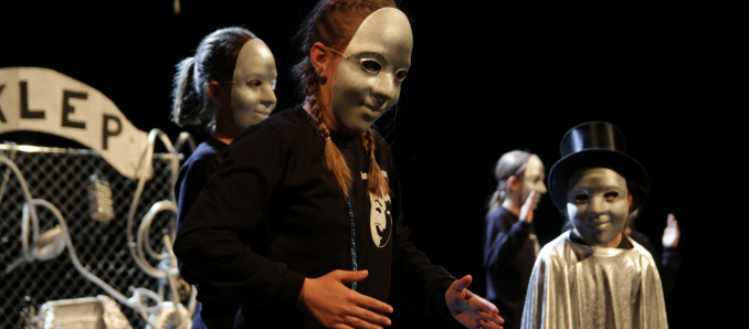 kilka osbób na scenie z maskami teatralnymi