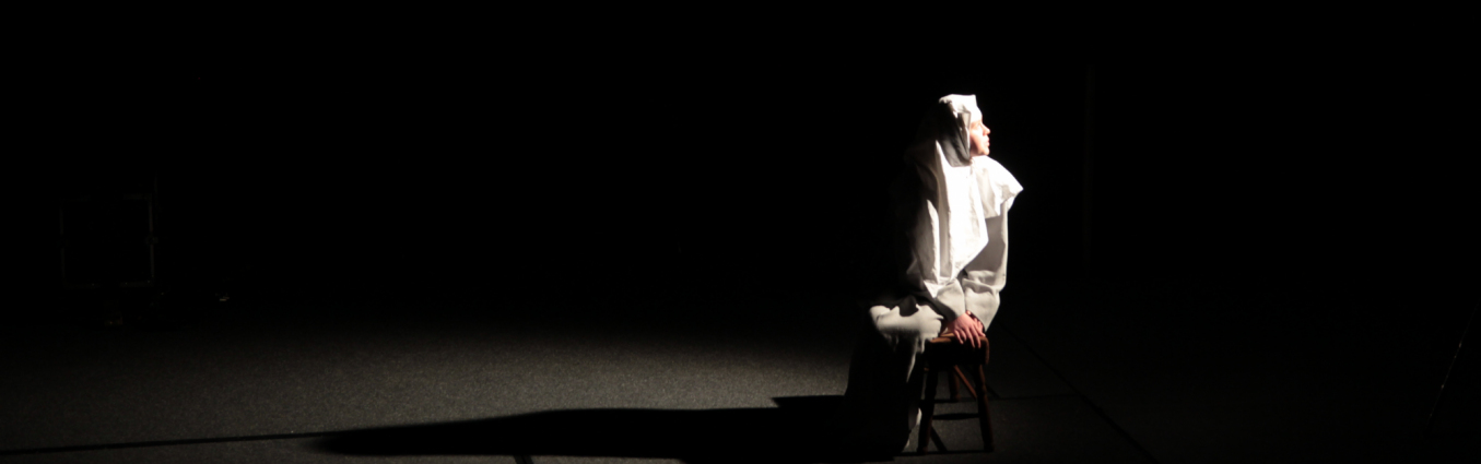 Osoba ubrana w białe szaty siedzi na krześle w świetle reflektora