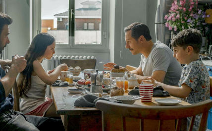 Dwóch mężczyzn i dwoje dzieci siedzą przy stole z napojami i jedzeniem.