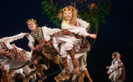 dzieci tańczące na scenie, na pierwszym planie podskakująca dziewczynka z wiankiem na głowie