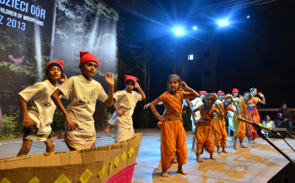 dzieci w hinduskich strojach stoją na scenie, oświetlają je światła sceniczne