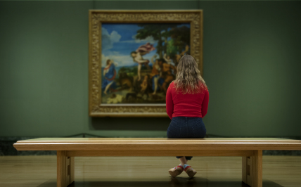Kobieta siedząca na ławce w muzeum wpatrująca się w obraz 