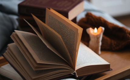 otwarta książka na stole, a obok świeca