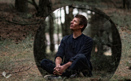 mężczyzna siedzi na trawie w lesie