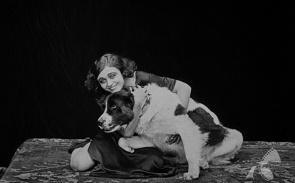 Czarno-białe zdjęcia. Kobieta siedzi na podłodze, uśmiecha się i przytula dużego psa.