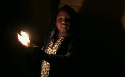Mały chłopiec w ciemnym pomieszczeniu trzymający zapaloną świeczkę