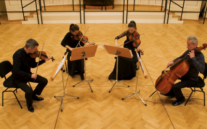 Czworo muzyków gra na instrumentach smyczkowych w sali z lustrami.
