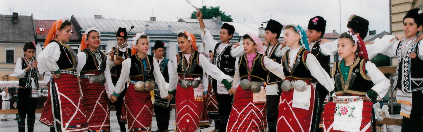 Dzieci w macedońskich strojach regionalnych tańczą na scenie.