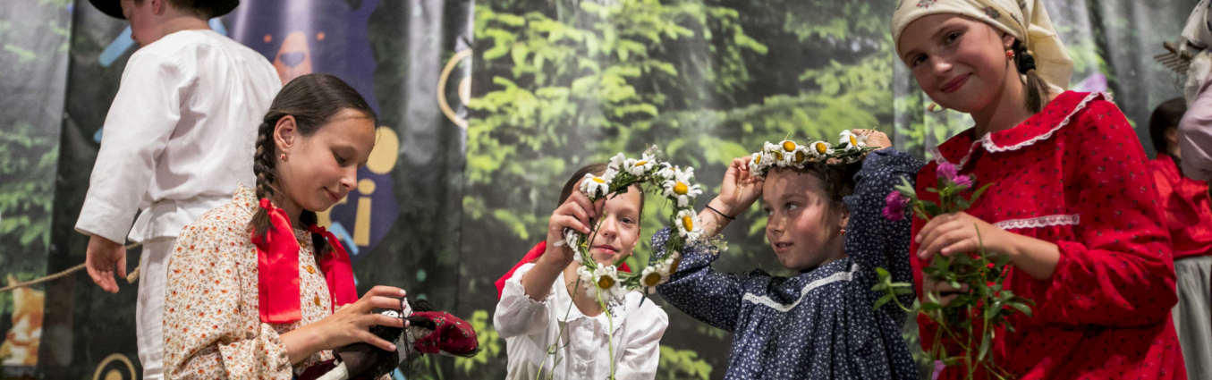 Grupa dziewczynek w strojach regionalnych, plecie kwiatki na scenie