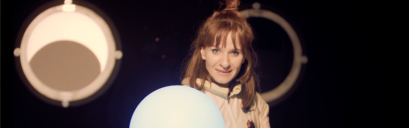 Kobieta w stroju kosmonauty trzyma w ręku świecącą kulę
