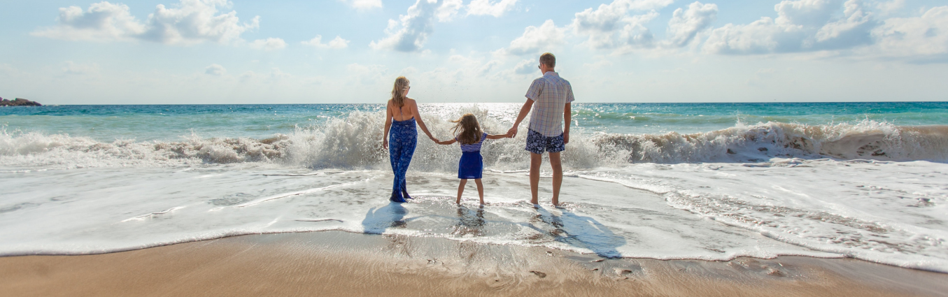 Rodzina trzyma się za ręce na brzegu plaży. Patrzą w stronę morza