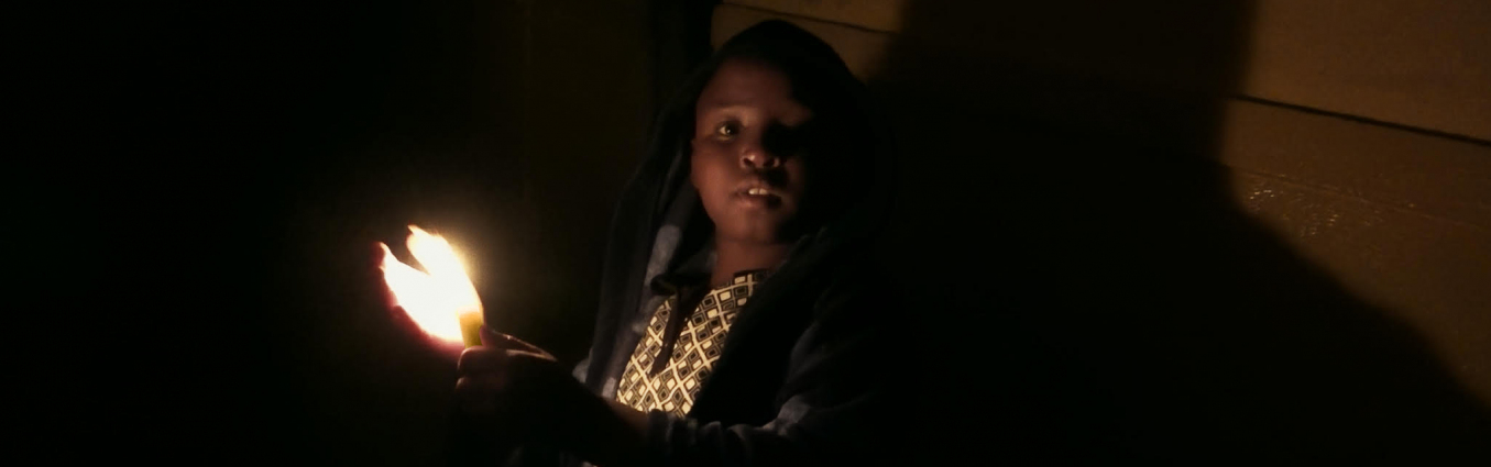 Mały chłopiec w ciemnym pomieszczeniu trzymający zapaloną świeczkę