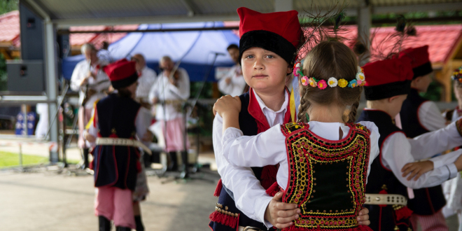 Chłopczyk i dziewczynka w strojach regionalnych z regionu krakowskiego tańczą na scenie