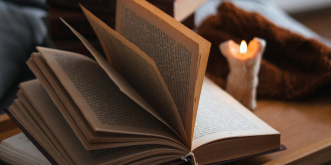 otwarta książka na stole, a obok świeca
