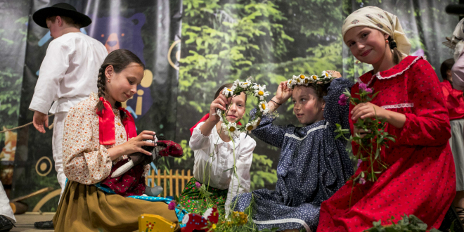 Grupa dziewczynek w strojach regionalnych, plecie kwiatki na scenie