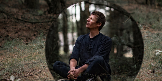 mężczyzna siedzi na trawie w lesie
