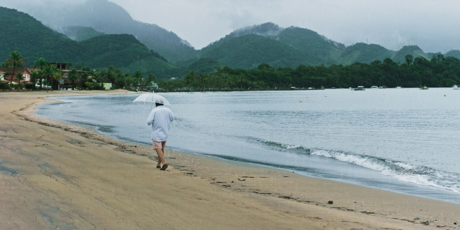 mężczyzna w koszuli spaceruje po plaży, w ręku trzyma parasol