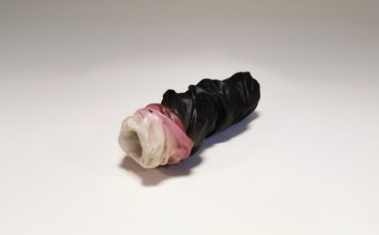 Niewielki owalny przedmiot - rzeźba, przypomina butelką, na którą naciągnięto dużą warstwę tkaniny, która się marszczy, tworzy zagłębienia. Obiekt jest prawie w całości czarny, jeden koniec biały. Między czarnym a białym kolorem występuje kolor różowy.