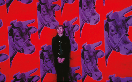 Na tle czerwonej tapety z wielokrotnie powielonym obrazem fioletowej, krowiej głowy stoi mężczyzna, artysta amerykańskiego pochodzenia – Andy Warhol. Mężczyzna stoi prawie na baczność, jego dłonie krzyżują się poniżej pasa. Beznamiętnie wpatruje się w kierunku fotografa wykonującego jego portret. Ubrany jest w czarnego koloru kurtkę oraz spodnie. Kurtka jest rozpięta i widać zielony podkoszulek. Na środku zdjęcia widnieje napis imitujący odręczny podpis Andy’ego Warhola.