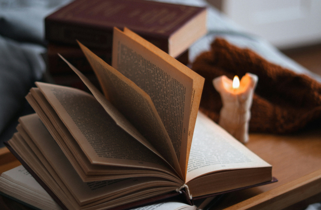 otwarta książka na stole, a obok świeca