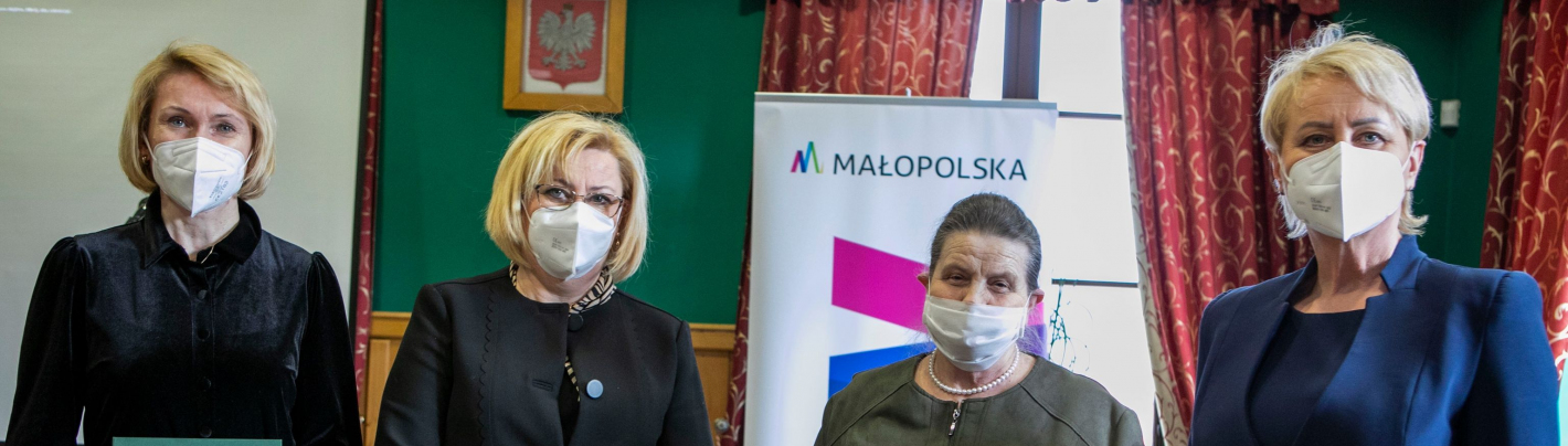 Cztery kobiety w maseczkach na twarzy stoją obok siebie. Dwie z nich trzymają w rękach dokumenty